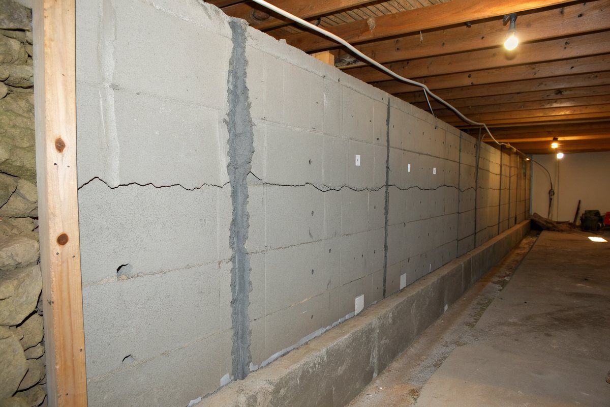 Long cracks across a concrete block basement wall under exposed ceiling joists