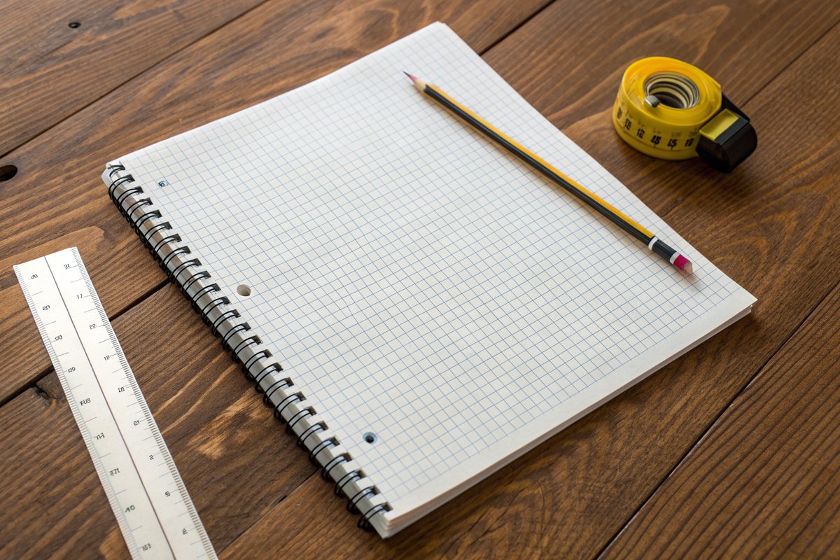 A blank graph-paper notepad, a pencil and a tape measure on a wooden table