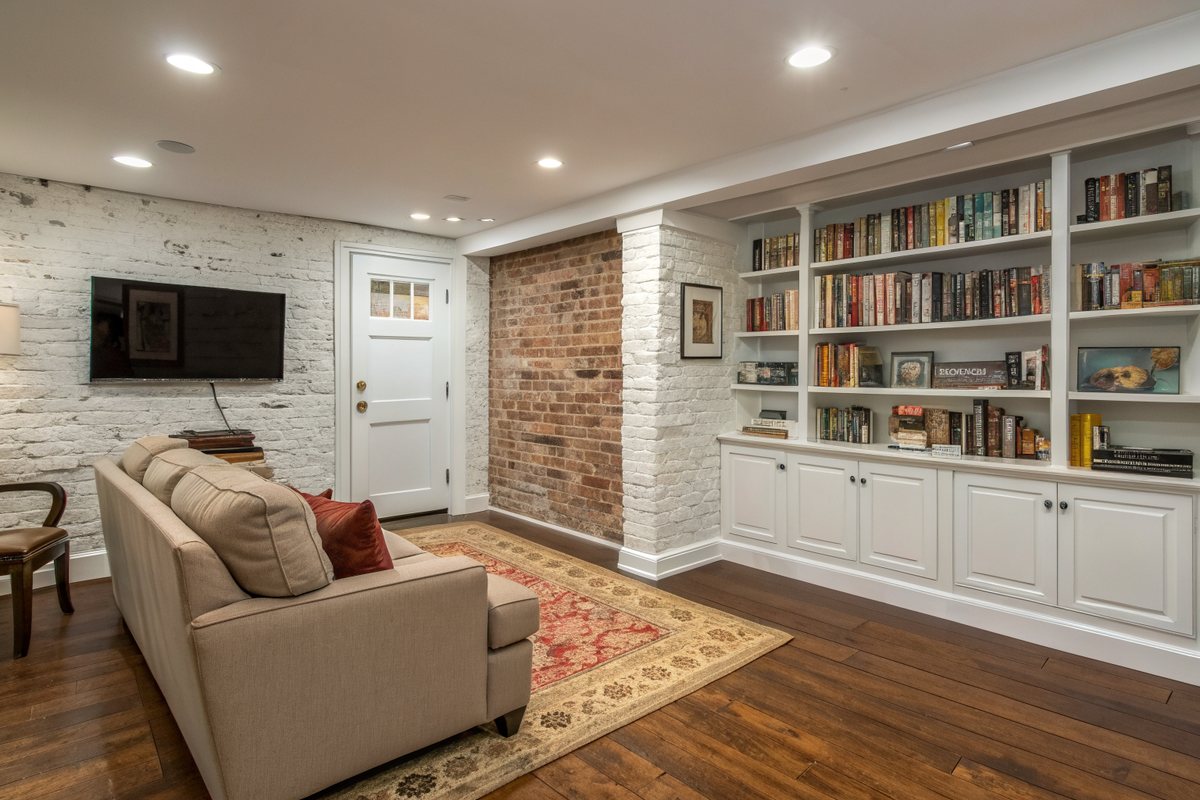 A dry finished rowhouse basement den with painted brick, a wood floor and bookshelves