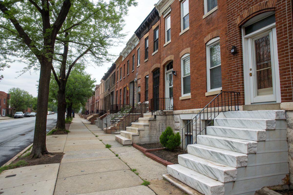 A row of brick rowhouses with white marble front steps and small basement windows at sidewalk level